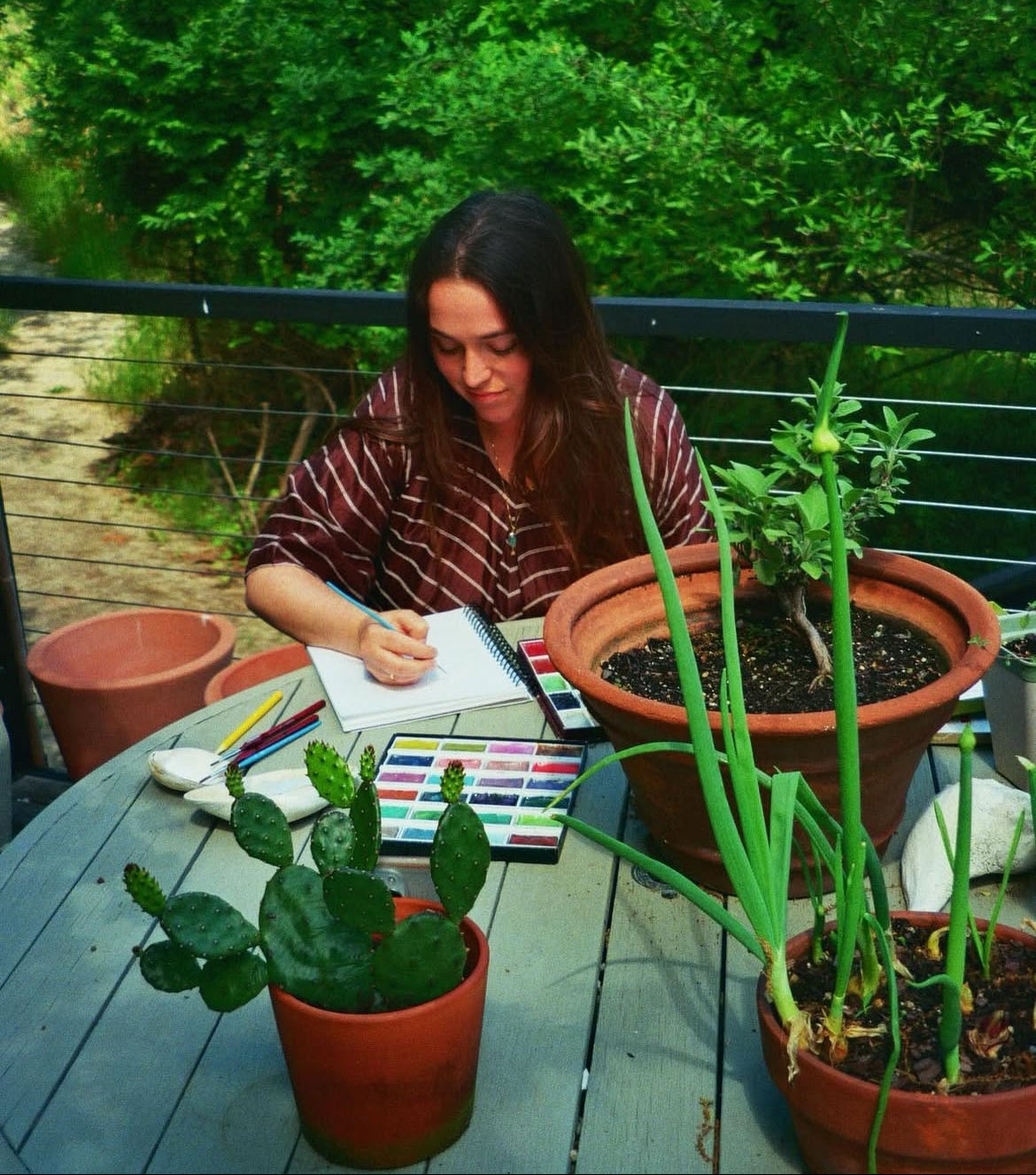 Woman sitting at a table with plants and art supplies outdoors